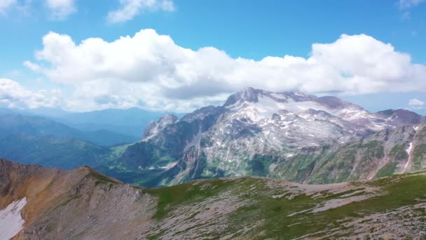 Widok z lotu ptaka od szczytu Oshten oszałamiającej majestatycznej natury Kaukazu do Mountain Fisht, pokryte śnieżnymi kamieniami i trawą pod białymi chmurami na błękitnym niebie. Zachód słońca w lecie, Adygea, Rosja — Wideo stockowe