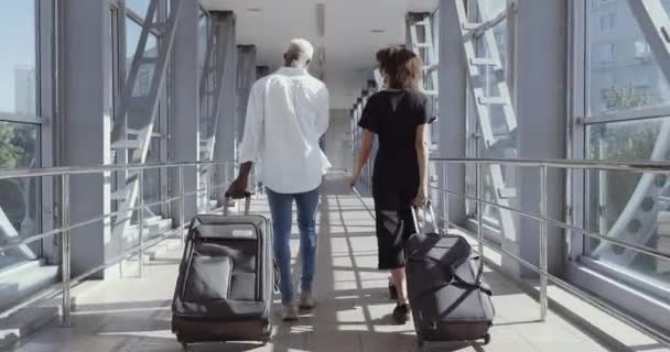 バケーション旅行に行く空港で一緒に歩いてアフロアメリカのカップルのバックビュー。一緒に旅行して。バックパックとスーツケースを持って。魅力的な若いです女性と男とともにスーツケース準備のために旅行 — ストック動画