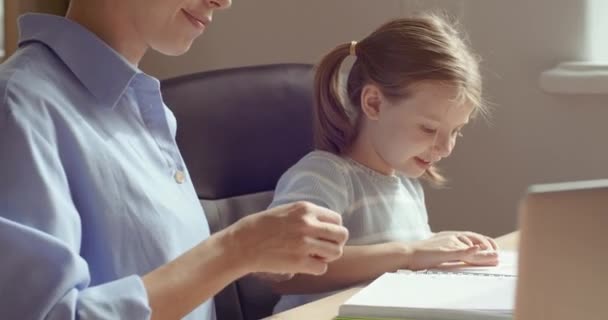 Jonge moeder helpt kleine dochter leunend online thuis op laptop. Twee mensen die samen praten terwijl ze huiswerk maken in de woonkamer met geluk, tijd samen doorbrengen, online onderwijs concept. — Stockvideo