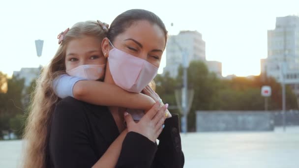 Kvinna i medicinsk mask, mamma håller barn i händerna på tillbaka på gatan promenad i coronavirus epidemi, titta kärleksfullt på kameran, stöder skyddar barnet. Mamma kramar dotter i pandemisk respiratoriskt virus risk — Stockvideo