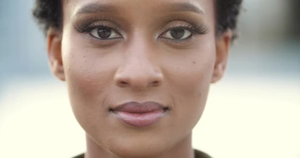 Voorzijde close-up van vrouwelijke gemengde ras mooi jong menselijk gezicht met donkere ogen en zwarte huid, serieus kijken naar camera openlijk en vol vertrouwen, pensive look, poseren charmant Afrikaans model, portret — Stockvideo