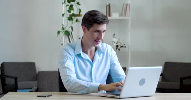 Homem caucasiano atraente sentado com laptop digitando sorrisos na câmera mostrando mão OK sinal. Millennial freelancer estudante aprendizagem on-line mostra tudo bem sucesso gesto linguagem corporal com o dedo — Vídeo de Stock