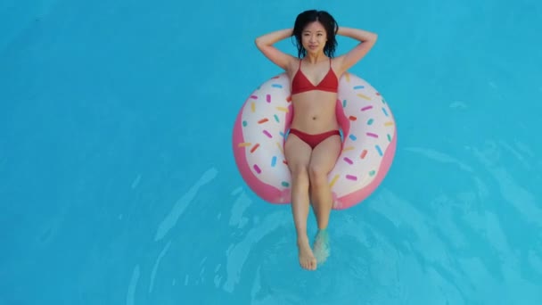 Japon öğrenci yaz tatilinde ev havuzunda dinleniyor. Asya uyruklu genç kız şişme halka donutun içinde yüzüyor, yüzüyor, kameraya güzel ve arkadaş canlısı görünüyor. — Stok video