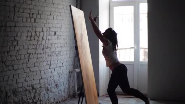Mladá žena, bystrá, talentovaná, tančící, skákající před oknem vytváří obraz kombinující malbu s tancem. Současné umění kombinující různé techniky a způsoby sebevyjádření — Stock video