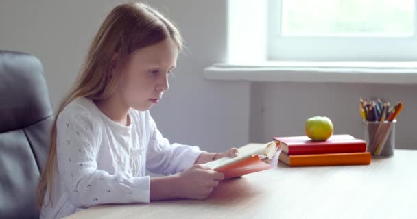 Schattig gericht schoolmeisje klein kind zit aan tafel thuis in school in de klas, leest boek hardop, doet huiswerk, bereidt examen test, leert door haarzelf tijdens quarantaine van pandemie virus — Stockvideo