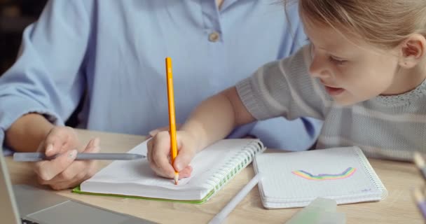 Közelkép egy kislányról, aki az anyjával ül az asztalnál, a gyerekek a kezükkel jegyzetfüzetbe rajzolnak fényes színű ceruzákkal, óvodások házit csinálnak, a család együtt tölti az idejét. — Stock videók