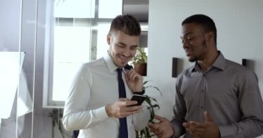 Ofis koridorunda yan yana dururken cep telefonuna bakan gülümseyen iki iş arkadaşı. İki iş arkadaşı akıllı telefondan komik videolar izliyor, iş yerinde öğle arasında konuşuyor.