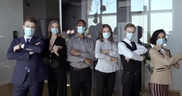 Gemotiveerde multidimensionale business team staat samen in de vergaderzaal, zelfverzekerde collega 's vouwen armen over borstkas, kantoormedewerkers dragen beschermende medische maskers te voorkomen virus, veiligheid concept — Stockvideo