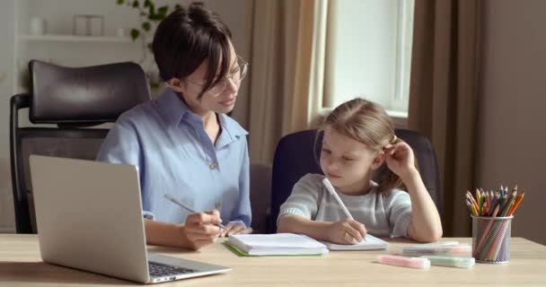 Aranyos kis óvodás lány gyerek lánya tanul írni a fiatal anya tanár. Felnőtt szülő anya tanít iskolás gyermek segít a házi feladatot tanul ül otthon asztal. A gyermeknevelés fogalma — Stock videók