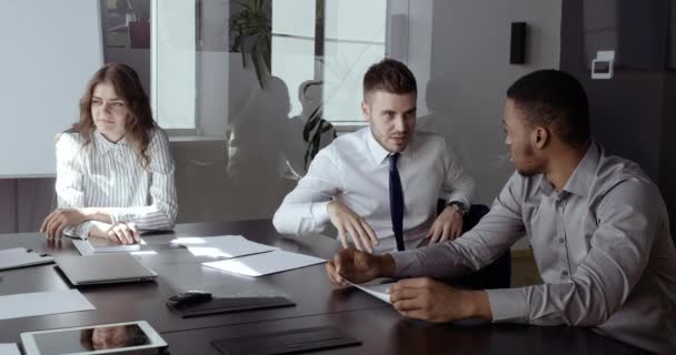 Twee mannelijke collega 's en bedrijfsleider zitten aan tafel in de pauze tussen twee conferenties. Blanke man toont handgebaar aan Afrikaanse werknemer manager, actief uitleggen mening — Stockvideo