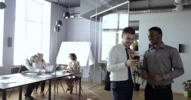 İki gülümseyen iş arkadaşı koridorda durup telefonda komik videolara bakıyorlar, gülüyorlar, iş yerinde eğleniyorlar. Afrikalı işadamı ile Milenyum çalışanı resmi olmayan bir ortamda iletişim kuruyor.