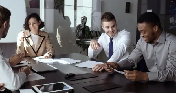 Groep slimme multiraciale jonge managers kantoormedewerkers die aan tafel zitten in de vergaderzaal, zich voorbereiden op een ontmoeting, grappen maken, samen praten tijdens de pauze van het werk, projectidee bespreken — Stockvideo