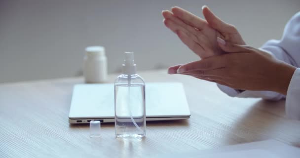 Femme médecin assis à table traite ses mains avec un désinfectant, nettoie ordinateur portable avec de la lotion liquide antibactérienne. Gros plan des bras féminins stérilité lavage des bactéries. Risque d'infection par le virus covidé — Video