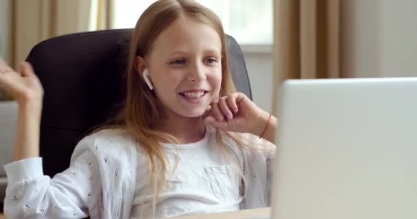 Rubia adolescente lleva auriculares, se sienta a comer mesa en casa, mira a la computadora portátil, se comunica en videollamada, habla con la webcam, se comunica de forma remota con la familia o amigos de la escuela durante la pandemia de cuarentena — Vídeo de stock