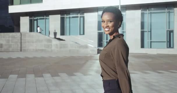 Mulher africana elegante usa roupas de moda clássica, penteado curto, sorri olha em volta para a câmera, gosta de verão depois de chegar ao terminal do aeroporto, anda rua, passos em telhas perto do edifício da cidade — Vídeo de Stock