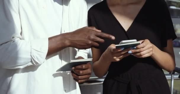 Zblízka lidské ruce drží vstupenky, mužské prsty ukazují na obrazovku mobilního telefonu. Pár afrických přátel nosí masky stojí při sobě, žena s smartphonem hledá informace na netu — Stock video