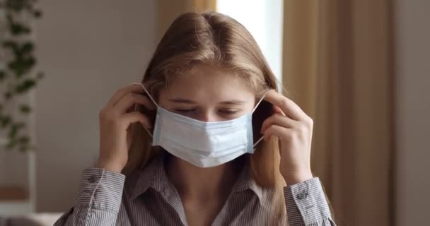 Πορτρέτο της νεαρής ελκυστική κοπέλα βάζει σε ιατρική μάσκα στο πρόσωπό της. Headshot φοιτητής γυναίκα προστατεύει την υγεία από την αναπνευστική νόσο του ιού covid, κίνδυνος μόλυνσης από τον ιό της στέψης, πανδημία χρόνο επιδημίας — Αρχείο Βίντεο