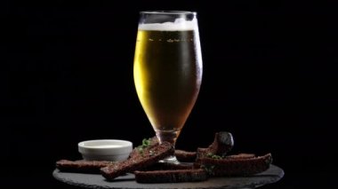 Bir bardak alkolsüz, soğuk, hafif, koyu bir bira ya da bira. Bar kafeteryasında, ekmek kızartmasının yanında, mutfak masasında duruyor. Hafta sonu kaçamağı konsepti, erkek eğlencesi örneği.