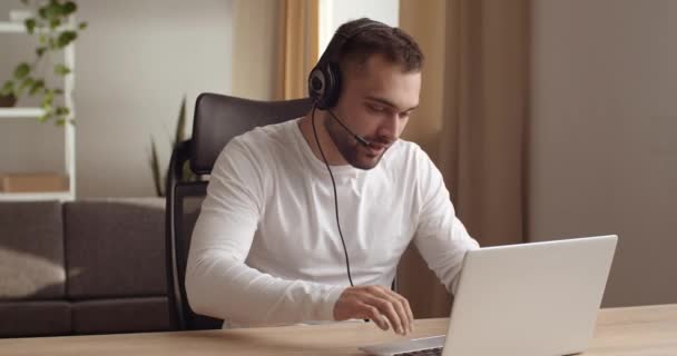 Homem de negócios agente freelancer gerente de chamadas usa fones de ouvido microfone cabeça olha para a tela do laptop digitação no teclado do computador funciona on-line aprende boas notícias se alegra com sucesso ou ganhar recebe aprovação — Vídeo de Stock