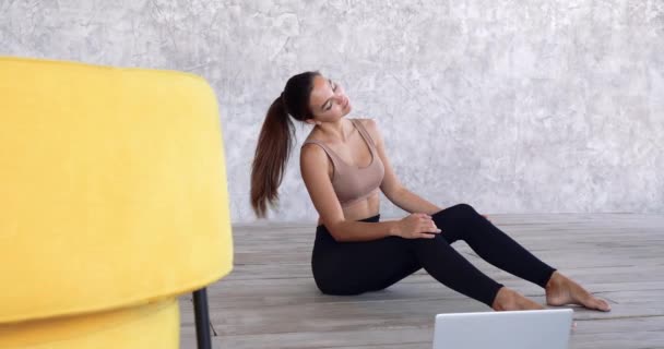 소녀 조련사나 무용수 여자 혼자 방에 앉아 노란색의자 가까이 바닥에 앉아 있고, 목에 통증을 느끼고, 등에 운동을 하고, 머리를 양 옆으로 기울이는 근육을 당기고, 온라인으로 노트북을 보는 훈련을 한다. — 비디오