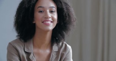 Mutlu melez kız kameraya geniş dişli bir gülümsemeyle bakıyor, önünde elini kaldırıyor, işaret veriyor, parmaklarını sıfıra katlıyor, kafa sallıyor, göz kırpıyor, onay konseptini onaylıyor.