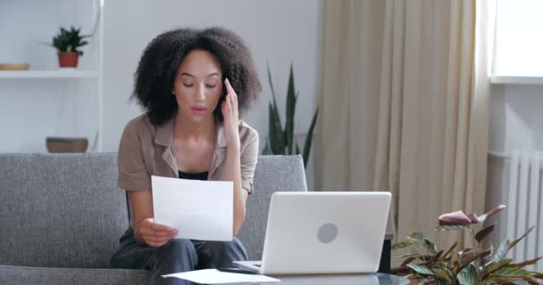 Afro-Américaine adolescente étudiante diplômée s'assoit à la maison dans la chambre sur le canapé, lit le texte d'information, fait des devoirs laborieux, ne peut pas trouver de solution, prendre des notes, se sent irritée fatigue tristesse — Video