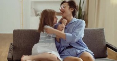 Mutlu anne portresi ve küçük tatlı kız kızı gıdıklanıyor kanepede uzanıyor, gülüyor, kaygısız annecilik oynuyor sarılmaktan hoşlanıyor küçük komik çocukla vakit geçiriyor.