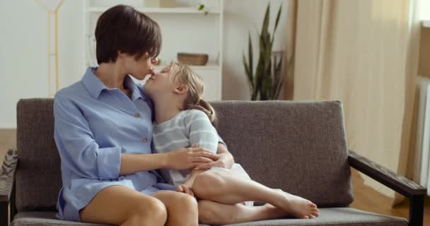 Bonito adorável engraçado criança pequena filha abraços e beijos jovem mãe, família jogando no sofá em casa, mãe feliz e pequena criança menina desfrutando de ligação passar tempo juntos relaxar se divertindo no sofá — Vídeo de Stock