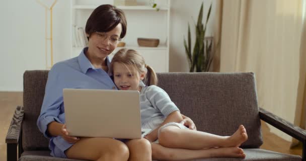 Glad förälder mamma och söt liten barn dotter två personer tittar på bärbar skärm webbkamera ha kul att göra konferens videosamtal chatta eller lära sig tillsammans hemma koppla av skrattar sitter på soffan — Stockvideo