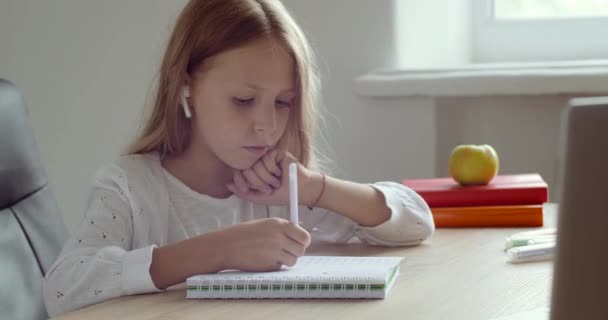 Ernsthaft fokussierte Schülerin sitzt zu Hause am Tisch und trägt Kopfhörer, winkende Hand grüßt Online-Lehrer nickt mit dem Kopf, macht Hausaufgaben, schreibt Notizen, studiert aus der Ferne über E-Learning während der Coronavirus-Pandemie — Stockvideo