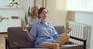 Dikkatli, sakin bir anne evdeki kanepede oturup meditasyon yaparken gürültülü, aktif bir kız çocuğu zıplayarak oynarken, anne evde yoga egzersizi yaparken küçük çocuk bağırdığında stres atlamak için