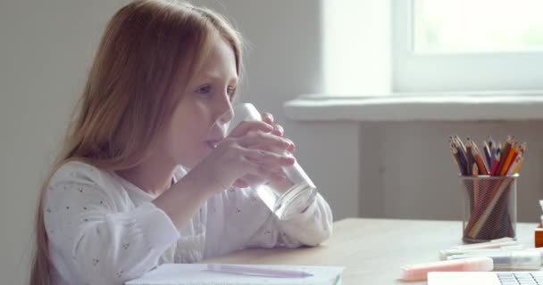 Colegiala se sienta en casa mesa toma un descanso durante la tarea, se siente sediento recoge vidrio transparente de agua fría limpia filtrada no carbonatada toma un gran sorbo refresca con bebida, concepto de e-learning — Vídeos de Stock