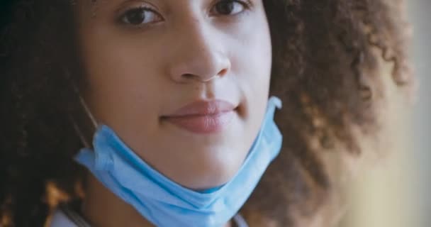 검은 곱슬곱슬 한 머리를 하고 있는 아프리카계 미국인젊은 여성의 얼굴에 마스크를 쓰는 여성의 근접 사진, 열렬 한 바이러스 감염으로부터 입과 코를 보호하는 혼합 인종 여성, 전염병과 세계적 인 개념 — 비디오