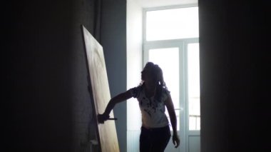 Güzel modern kadın sanatçı stüdyoda parlak, sıra dışı, soyut bir tablo yaratıyor. Kız çalışırken farklı teknikleri birleştiriyor, yağlı boya kullanarak tuvale geniş ve kalın vuruşlar uyguluyor.