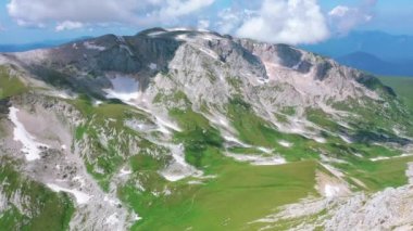 Beyaz bulutların altında kar taşları ve çimlerle kaplı Kafkasya 'nın görkemli doğasının Oshten tepesinden Mountain Fisht' e kadar uzanan hava manzarası. Güneş yazın ışıldıyor, Adygea, Rusya