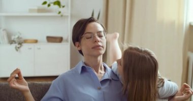 Annesinin gözlüklü portresi. Kanepede oturmuş poz veriyor. Kız meditasyon yapıyor, annesinin yanına koşuyor.