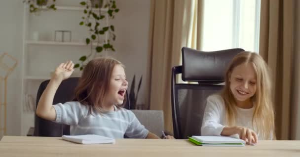 Две милые маленькие школьницы пара дошкольных детей подружки, сидящие за столом стола в школе или дома исследования дистанционно рисовать написать смех дать пять рук символ согласия знак успеха — стоковое видео