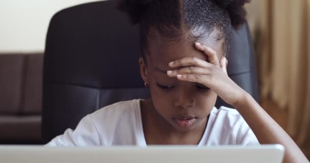 Vista frontal del niño afroamericano niña triste poco molesto sentado en el ordenador portátil mirando la pantalla haciendo tarea en línea estudiar remotamente sensación de estrés problema agarrar la cabeza con las manos — Vídeos de Stock