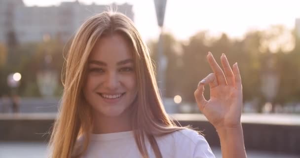 Venku portrét atraktivní mladé tisícileté dívky se usmívá na fotoaparát ukazující ruku ok znamení. Kavkazská dáma předvádí všechno, co umí, gesto úspěchu, řeč těla. Zblízka žena úsměv při pohledu do kamery — Stock video