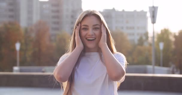 Retrato de modelo estudante jovem feliz com cabelos longos em pé ao ar livre com rosto surpreso sente choque alegria prazer agradavelmente de boas notícias positivas cobrindo sua boca com as mãos diz wow — Vídeo de Stock