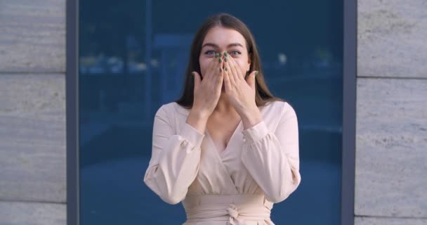 Retrato de jovem morena estudante menina com cabelos longos está posando olhando para a câmera se sente agradável choque e prazer, fecha a boca com as mãos em admiração e surpresa, rosto feminino feliz — Vídeo de Stock