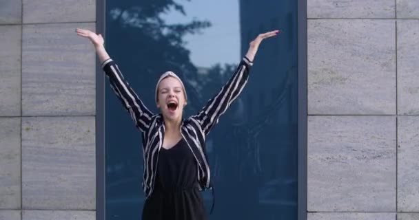 Jeune femme séduisante modèle étudiant se tient dans la rue devant la caméra sent triomphe joie crie bruyamment avec bonheur lève les mains vers le haut en sautant victorieusement dans l'air, concept de célébration du succès — Video