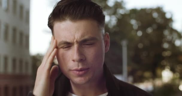 Retrato de rosto masculino triste, close-up do homem que sofre de dor de cabeça enxaqueca sente dor de cabeça condição, estudante sentindo-se doente segurando a cabeça com as mãos, esfrega suas têmporas com os dedos, close-up — Vídeo de Stock