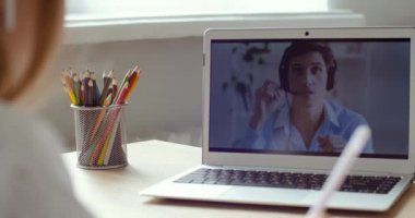 Genç liseli kız bilgisayarlı ekranda online öğretmenle uzaktan öğrenim konuşması yapıyor notlar yazıyor, hareketler tekrarlıyor. Erkek öğretmenle çevrimiçi konferans dersi, laptop ekranı. Omuz üstü görünümü