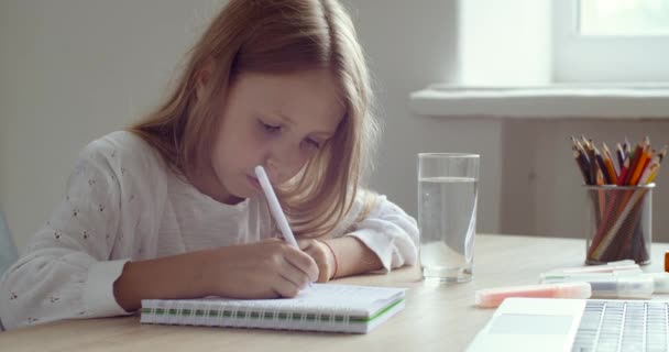 Gros plan petite écolière fait ses devoirs, écrit sur papier, étudie à distance de la maison en quarantaine en ligne, a soif, boit de l'eau minérale pure, boit, ferme les yeux avec soulagement — Video