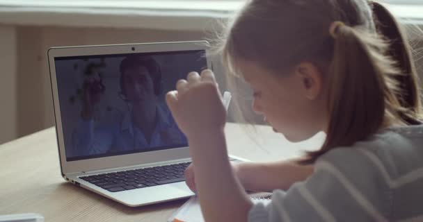 Kilátás hátulról kis óvodás lány ül az asztalnál otthon egyedül karanténban, nézi laptop képernyőn kommunikál tanár távolról online web cam tanul az e-tanulás során a vírusjárvány — Stock videók