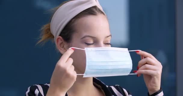 Крупный план женщины надевает синюю медицинскую защитную хирургическую маску на молодое женское лицо, портрет девушки-подростка в маске стоит на улице во время пандемического эпидемического вируса, закрывает рот и нос от инфекции — стоковое видео