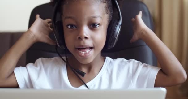 Fejlövés közelkép webkamera kilátás afro gyermek lány fülhallgató beszél mikrofonba, aktívan elmagyarázza érzelmileg integetett a kezét, kuplungok fejét a probléma, vicces kis gyerek kommunikálni online — Stock videók