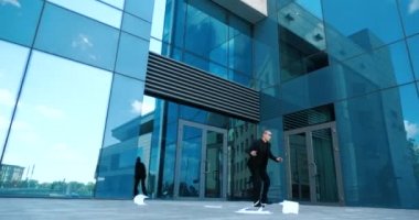 Ofis çalışanı toplantıya geç kalıyor, iş merkezinin yakınındaki kaldırımda dökümanları kaybediyor, rüzgar gazeteleri iki yana savuruyor, yönetici yerden dosya topluyor