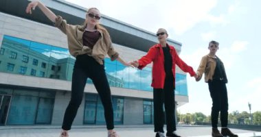 Dansçılardan oluşan oyuncu bir takım, dans eden üç şık genç öğrenci kollarıyla mavi cam iş merkezinin arka planında dalga hareketleri yapıyorlar. Neşeli bin yıllar, mutluluk ve olumlu hareket